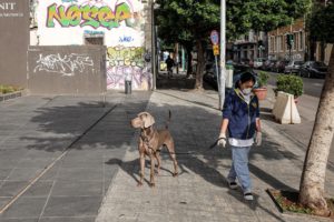 A masked domestic worker walks a dog along a quiet street in the Mar Mikhael district of Beirut. (Finbar Anderson)