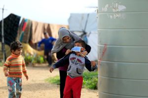 A Syrian refugee woman puts a face mask on a boy as a precaution against the spread of coronavirus, in al-Wazzani area, in southern Lebanon, March 14, 2020. (Reuters)