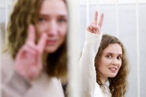 Belsat TV journalists Katerina Bakhvalova (R) and Daria Chultsova (L), who were detained in Nov 2020 while reporting on anti-government protests, embrace each other in a defendants' cage before the start of their trial in Minsk. (File photo: AFP)