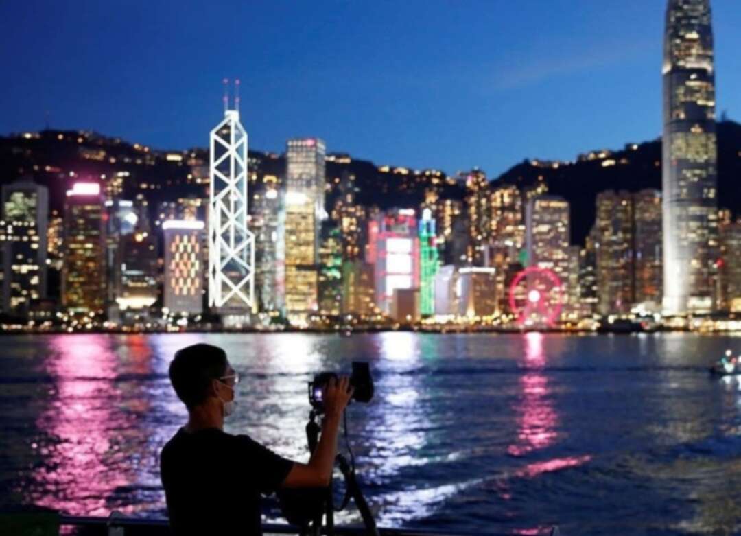 A man wearing a protective face mask takes a photo of the sunset at Tsim Sha Tsui waterfront as skyline buildings stand across Victoria Harbor following the coronavirus disease (COVID-19) outbreak in Hong Kong. (Reuters)