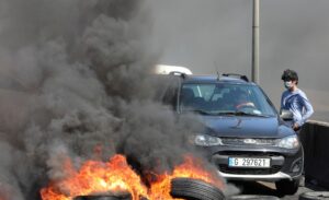 A woman tries to cross a blocked road with burning tires during a protest against the fall in Lebanese pound currency and mounting economic hardships in Khaldeh, Lebanon March 8, 2021. (Reuters)