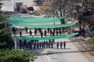 Police backed by soldiers advance on protesters holding a demonstration against the military coup, as heavy construction equipment (top) is used to dismantle a blockade, in Yangon on March 6, 2021. (File photo: AFP)